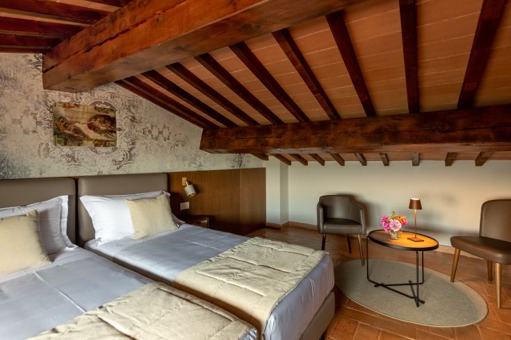 Einladender Innenraum mit sichtbaren Balken, bequemen Betten und einer gemütlichen Entspannungsecke mit Tisch und Blumen.