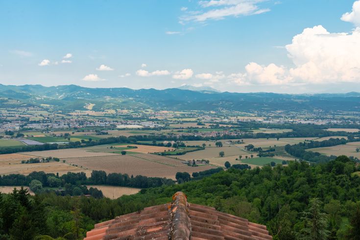 Eine Aussicht auf die hügelige Landschaft der Umbrien, mit grünen Feldern und Bergen im Hintergrund.