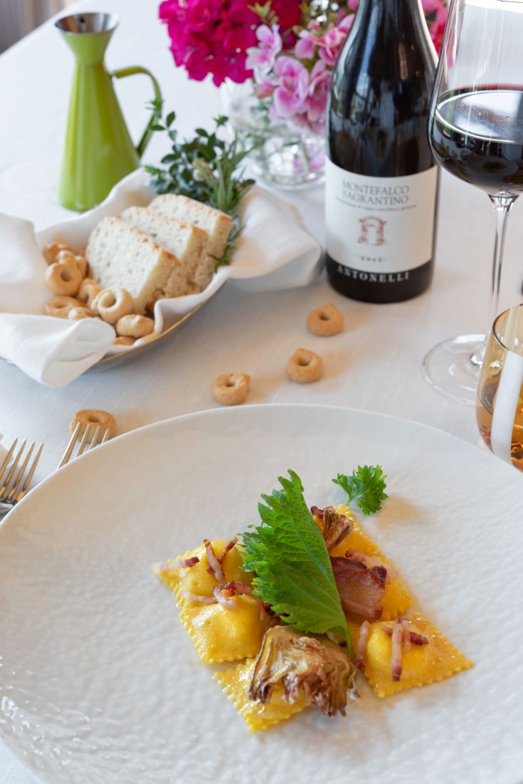 Ein Teller dekorierter Ravioli, serviert mit Rotwein und frisch gebackenem Brot.