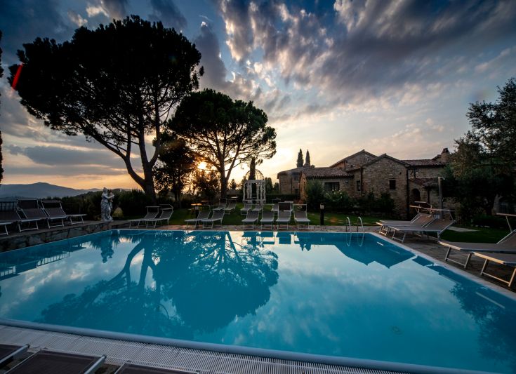 Ein ruhiger Pool umgeben von Bäumen, unter einem bunten Himmel bei Sonnenuntergang.