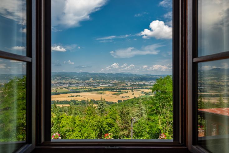 Innenszene mit Blick aus einem Fenster auf eine grüne Landschaft, klaren Himmel und weiße Wolken.