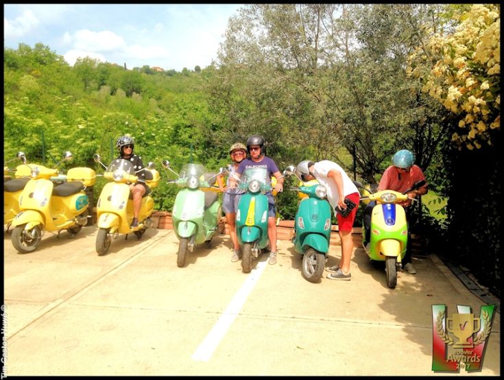 Un gruppo di persone su vespe di diversi colori in un paesaggio ricco di vegetazione tipica umbra.