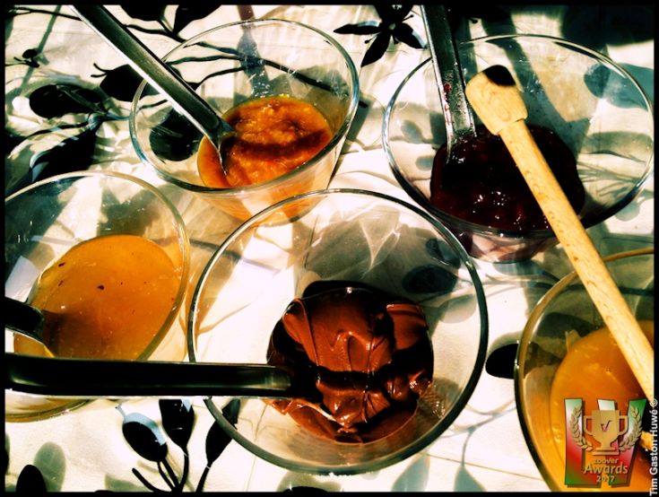 Cinque ciotole di marmellate dai colori vivaci, con uno stecchino di legno a disposizione. Un assortimento dolce.