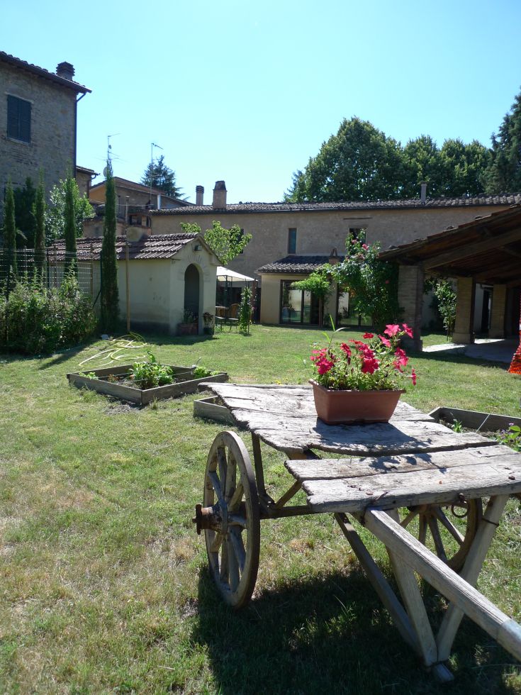 Un giardino caratterizzato da un vecchio carretto di legno e fiori variopinti, situato a Umbertide.