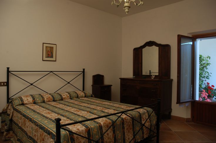 A simple bedroom with a double bed, overlooking a garden filled with flowers.