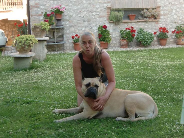 Une femme étreint un chien dans un jardin avec des plantes vertes et des fleurs colorées, entourée par la tranquillité de la nature.