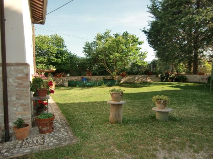 Jardin entourant un bâtiment rénové, immergé dans la végétation typique de l'Ombrie.