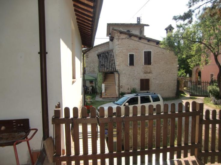 Ferme en pierre ombrienne, rénovée et entourée de verdure, proposant des appartements et des chambres pour des séjours paisibles.