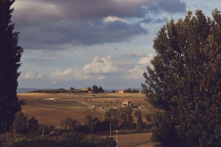Panorama collinare con abitazioni circondate dalla vegetazione e un cielo coperto di nuvole.
