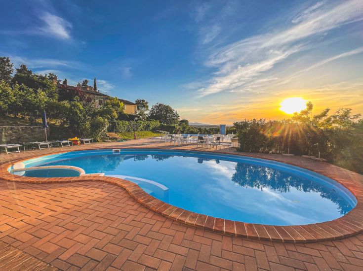 Scena della piscina al tramonto, immersa nella natura con colline verdi circostanti. Un luogo tranquillo per rilassarsi.