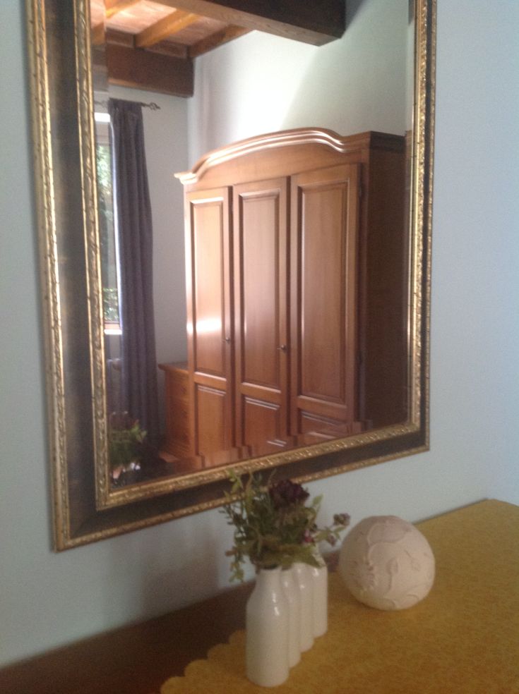 Specchio semplice che riflette un armadio in legno, alcune piante e un oggetto in ceramica.