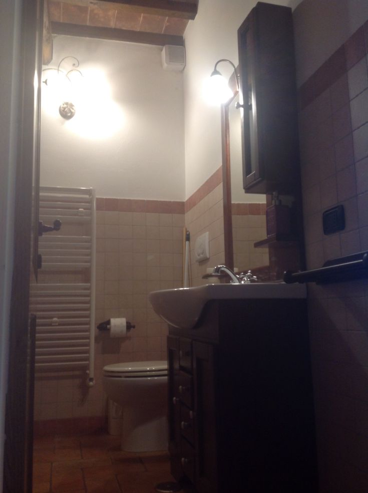 Un bagno sobrio con materiali ceramici, illuminato da una luce morbida e arredato in modo semplice.
