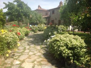 Un sentiero sereno attraversa fiori colorati e conduce a un edificio in pietra, immerso nella natura.
