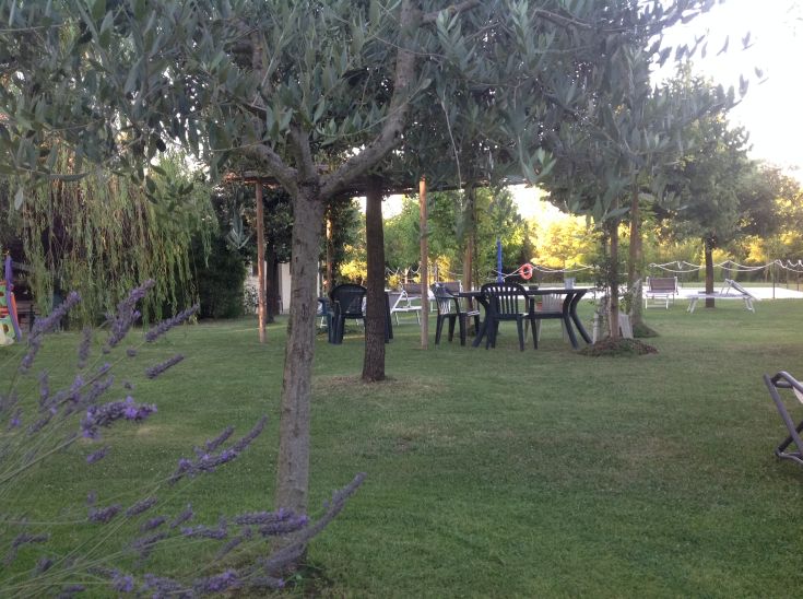 Area verde attrezzata con tavoli e sedie, circondata da alberi e fiori, adatta per momenti di relax e svago.