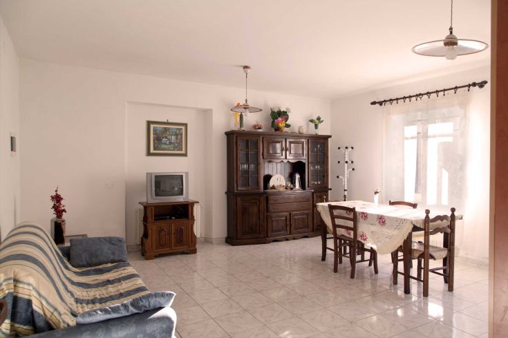 A cozy living room with wooden furniture and plenty of natural light. The atmosphere is sober and comfortable.