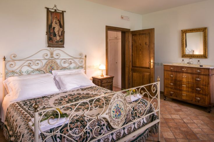 Camera semplice con letto in ferro battuto, elementi decorativi e buona illuminazione naturale.