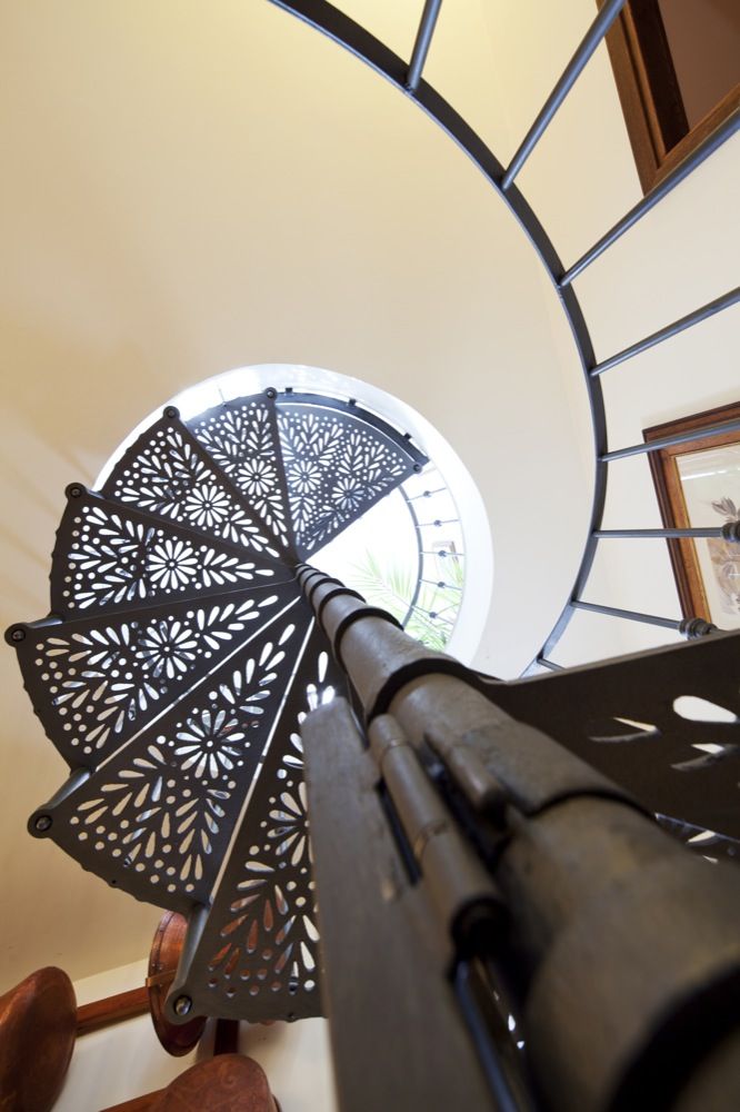 Scalinata in metallo a spirale che porta a un piano superiore, con dettagli semplici e una scena visibile attraverso una finestra rotonda.