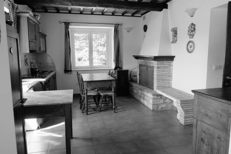 Traditional kitchen with a wooden table and stone finishes, illuminated by a large window.