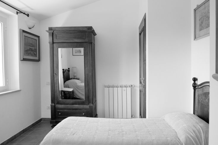 A simple and well-furnished room with a wooden wardrobe and a view of a green area.