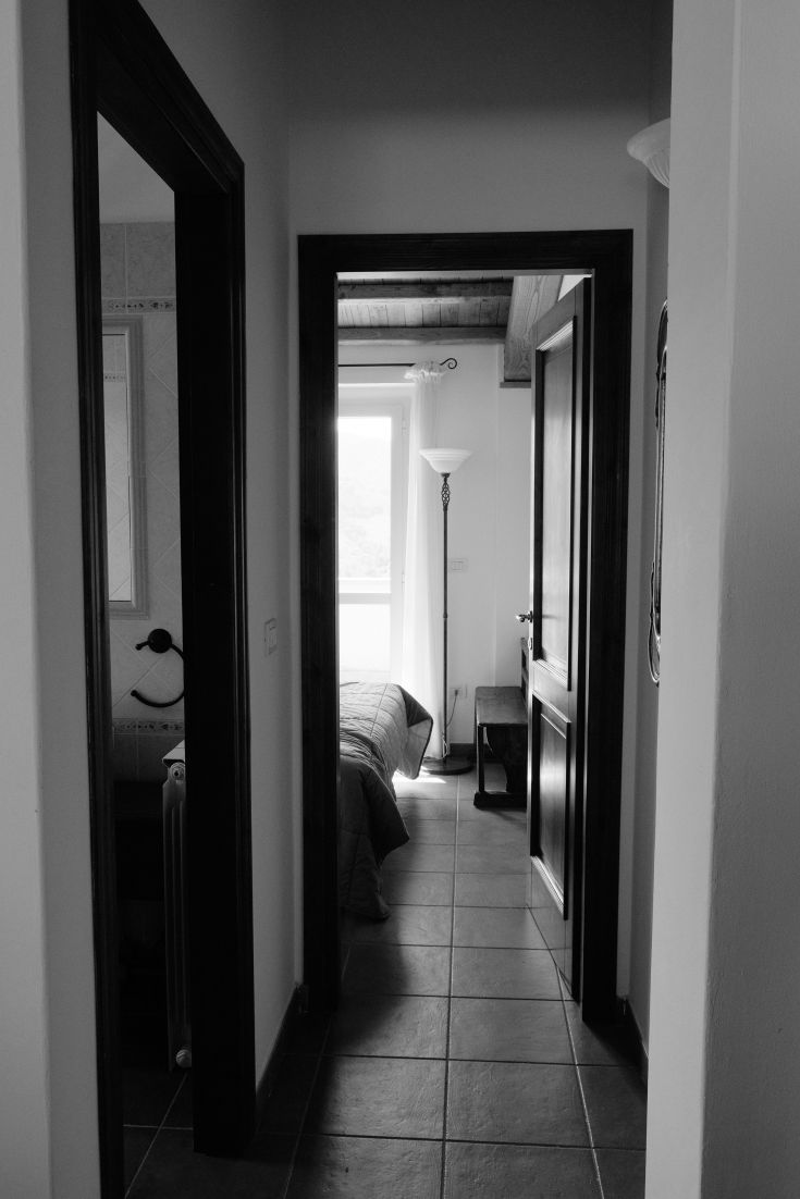 Interior of a building featuring a corridor leading to a room, with simple furnishings and natural light.