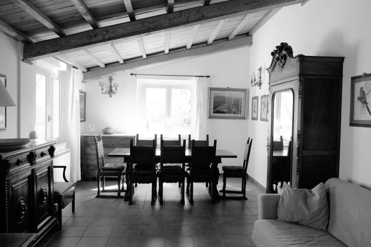 Interior of a historic farmhouse with a wooden table and chairs, beamed ceiling, and natural light illuminating the space.
