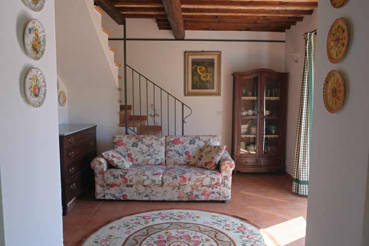 Simple living room with floral-patterned sofa, wooden stairs, and subtle decorations.