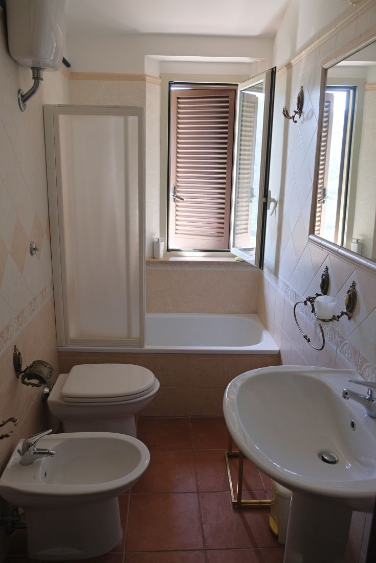 A simple bathroom with a bathtub and separate shower, illuminated by windows. The setting is tidy and inviting.