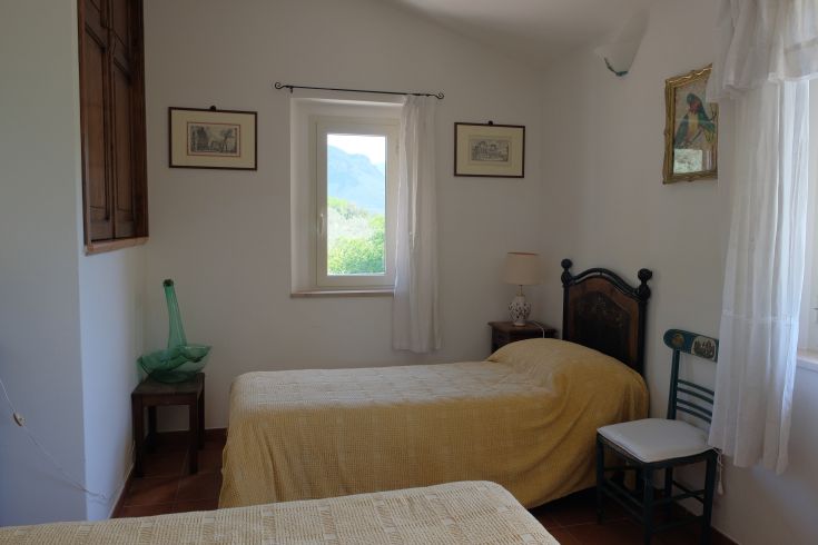 Bright room with single beds, simple furnishings, and a view of mountains and olive groves.