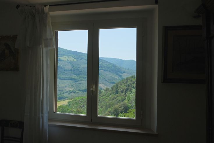 A window showcases a green hilly landscape, adorned with vegetation and surrounded by white tents.