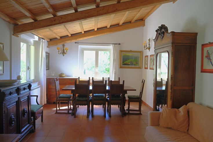 Spacious room with a wooden table and classic furniture, well-lit by windows overlooking the surrounding greenery.