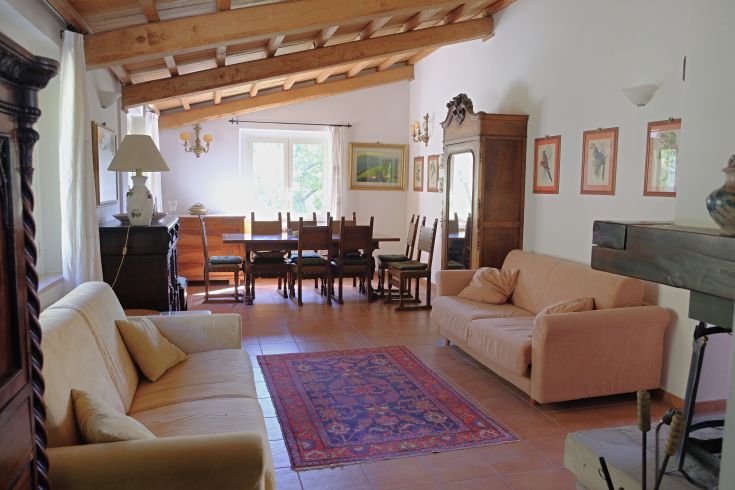 A spacious and cozy living room furnished with sofas and a large dining table, well-lit by windows.