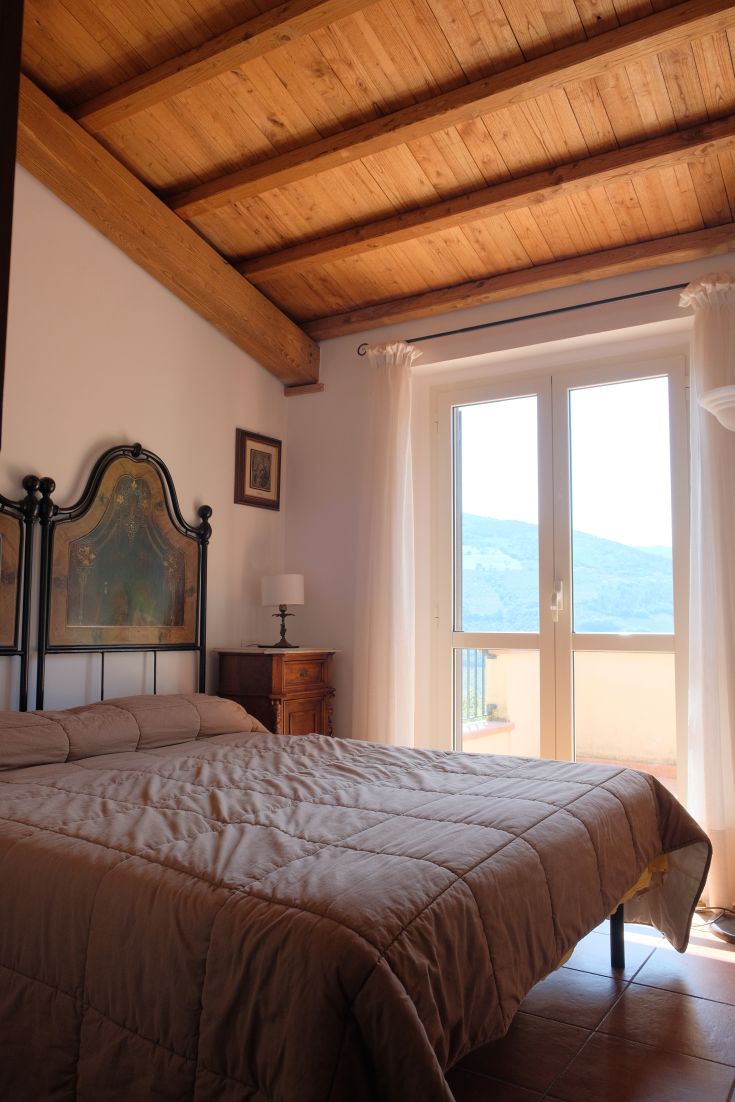 Spacious and bright bedroom with a double bed, simple furnishings, and natural scenery visible from the windows.