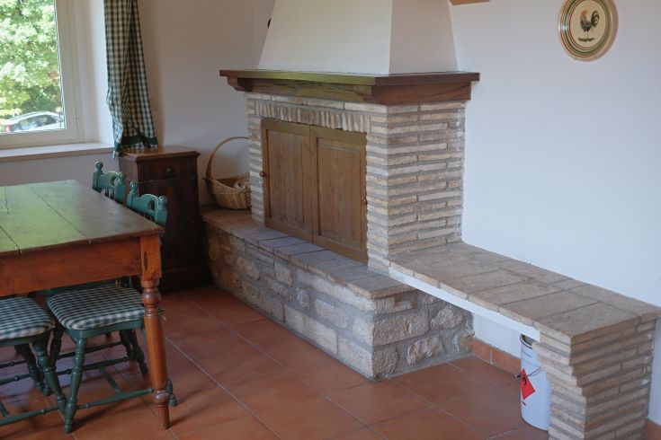 Inside a building featuring a stone fireplace and a wooden table. A cozy and simple atmosphere.