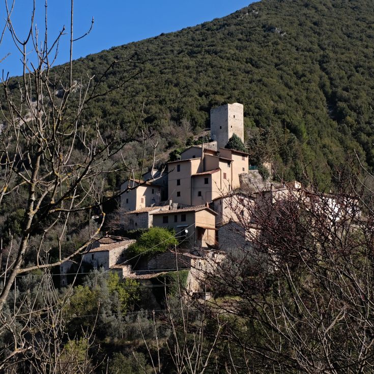 Historic stone building surrounded by greenery, featuring a pool and views of the Umbrian countryside.