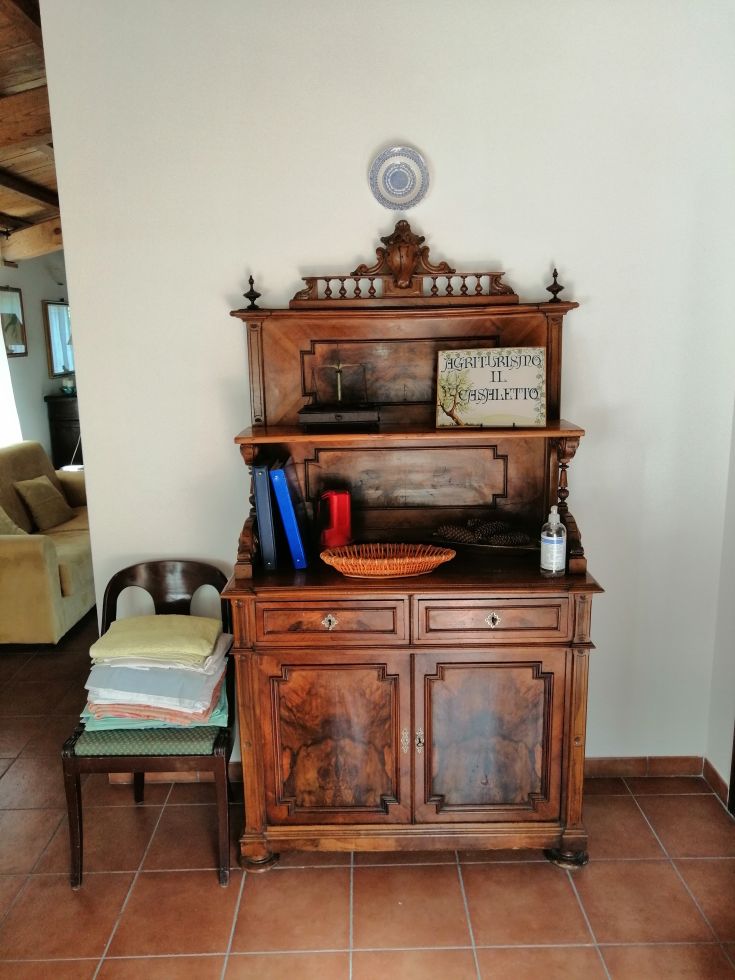 An antique wooden cabinet with simple details, adorned with colorful accessories. A plate hangs on the wall.