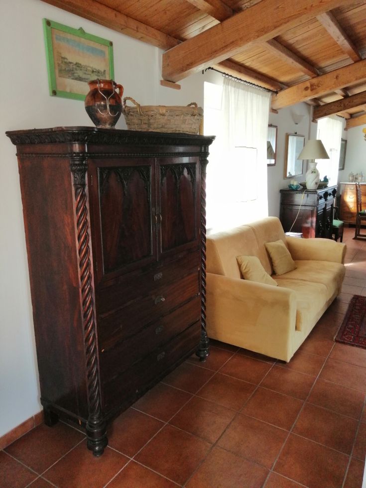 A simple rustic living room featuring a classic furniture piece and a yellow sofa, with exposed wooden beams.