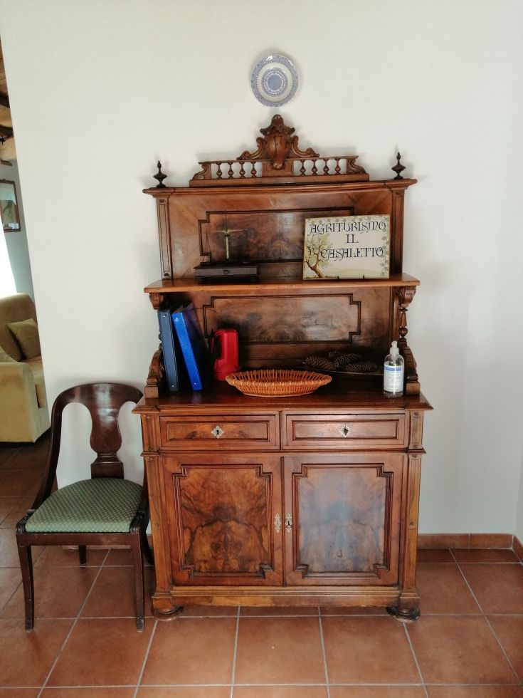A vintage wooden dresser with decorative details, next to a chair covered in green fabric.