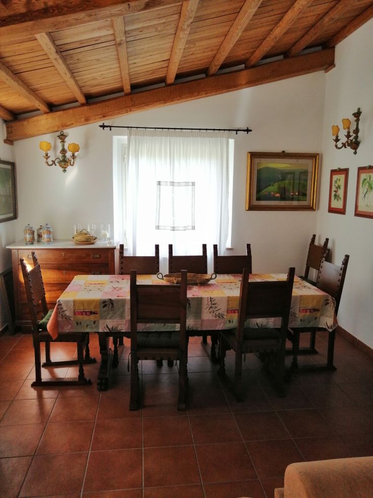 A cozy dining room with a long wooden table and chairs, brightly lit by large windows.