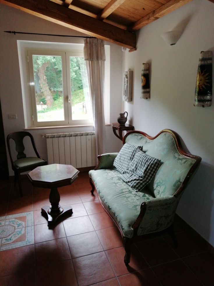 Furnished corner of a restored farmhouse in Valnerina, featuring simple furniture and a view of a green area.