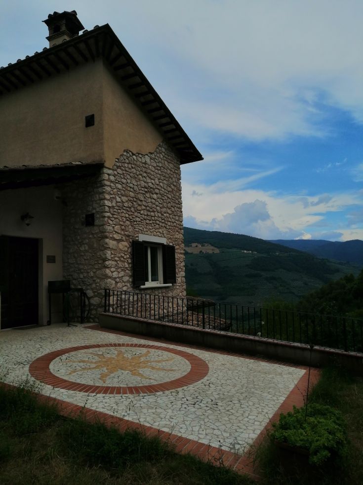 A renovated stone building surrounded by olive trees and greenery, overlooking the Valnerina.