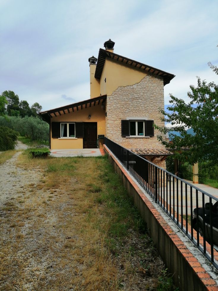 A restored farmhouse surrounded by olive trees in Valnerina, with a pool and panoramic views of the surrounding hills.