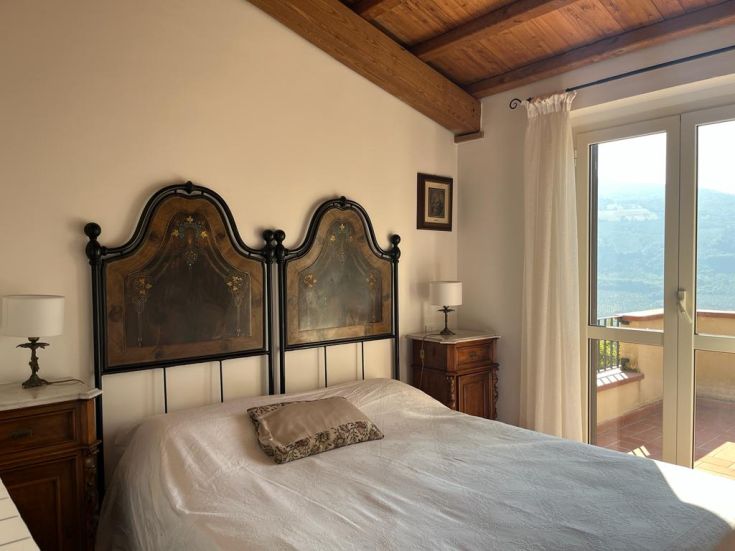 A room with a decorated bed, exposed beams, and a view of the surrounding landscape.