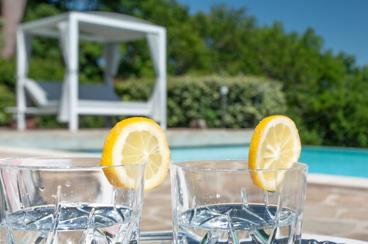 Bicchieri d'acqua al limone posati su un tavolo vicino a una piscina in un ambiente tranquillo.