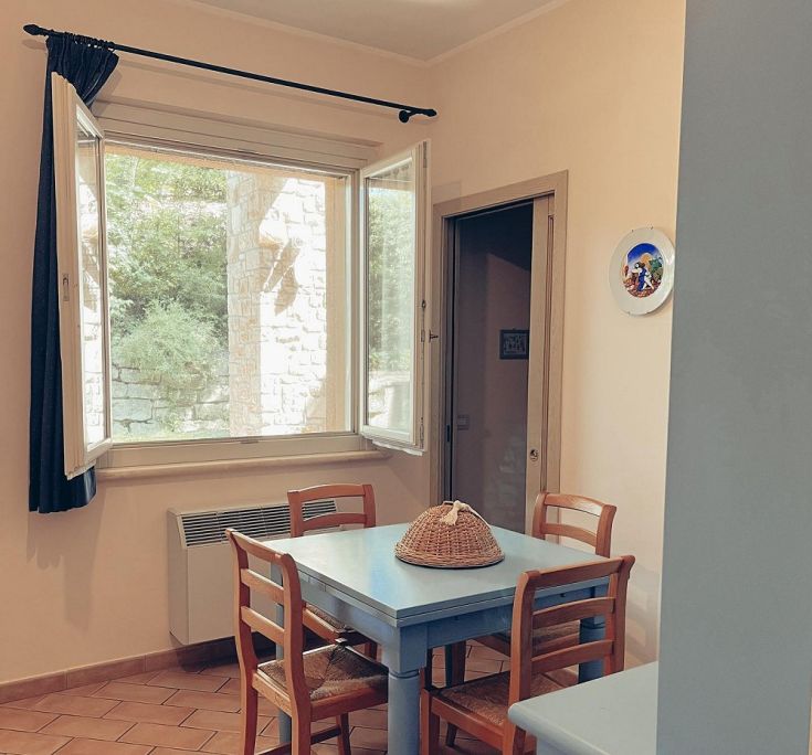 Ambiente familiare con tavolo, sedie in legno e una finestra ampia che rende lo spazio luminoso.