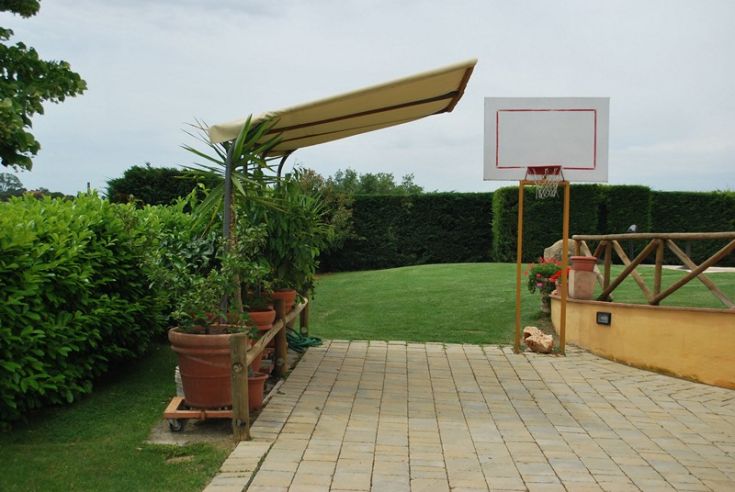 Eine Außenecke mit einem Basketballplatz, umgeben von grünen Pflanzen.