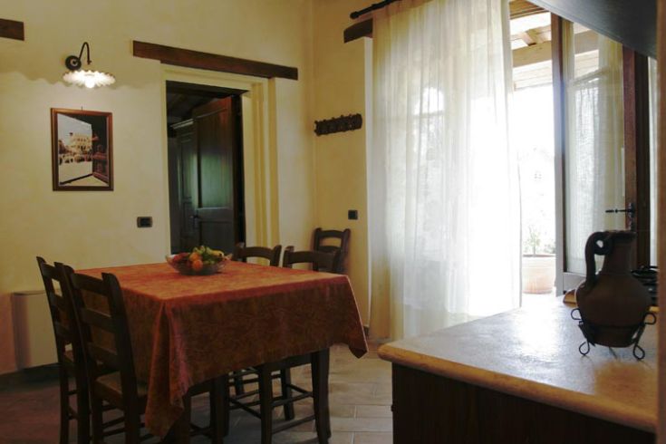 Interno semplice di un agriturismo con tavolo e panorama su un verdeggiato paesaggio umbro.