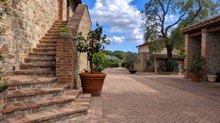 Angolo di un agriturismo con scale in pietra e aree verdi, immerso tra alberi e vegetazione.