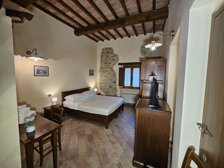 Camera confortevole in agriturismo, con arredi sobrii e panorama sulla vegetazione circostante.