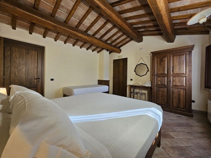 Camera ampia con letti e travi a vista, arredata in stile rustico, situata nelle colline umbre.