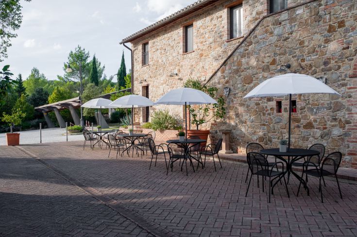L'area all'aperto di un agriturismo con tavoli e ombrelloni, immersa nel verde circostante.